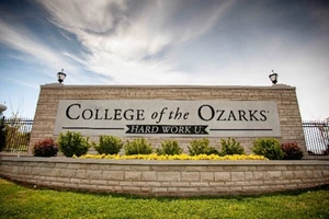 This picture depicts a stone sign with College of the Ozarks displayed boldly at its center. In front of the sign is a flower bed. 